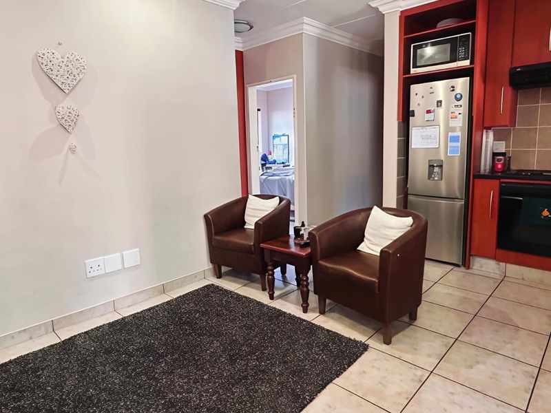Open-plan living area featuring a compact kitchen with built-in cabinetry, integrated appliances, and tiled flooring throughout.