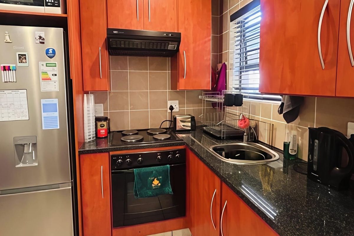 Compact kitchen featuring warm-toned wooden cabinetry, granite countertops, a built-in electric oven and hob, and a tiled backsplash.