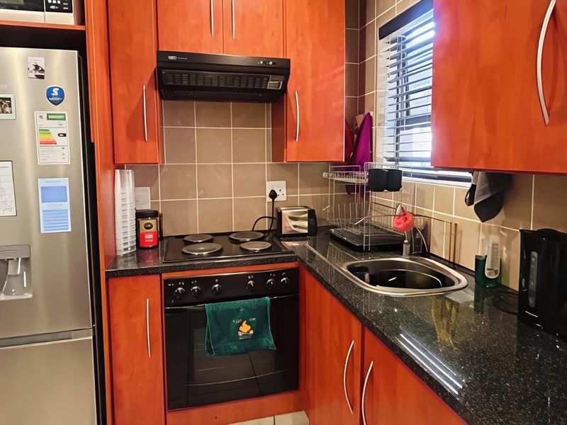 Compact kitchen featuring warm-toned wooden cabinetry, granite countertops, a built-in electric oven and hob, and a tiled backsplash.