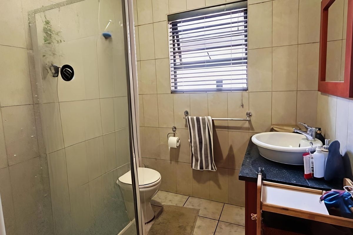 A functional bathroom featuring a glass-enclosed shower, vanity basin with granite countertop, and neutral wall tiling.
