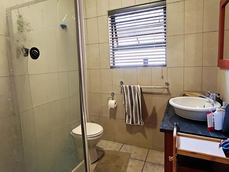 A functional bathroom featuring a glass-enclosed shower, vanity basin with granite countertop, and neutral wall tiling.