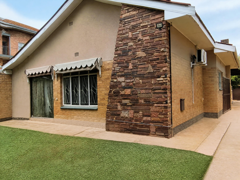 Rear exterior view of the house featuring a stone-clad feature wall, brick facade, paved walkway, artificial lawn, and window security bars.