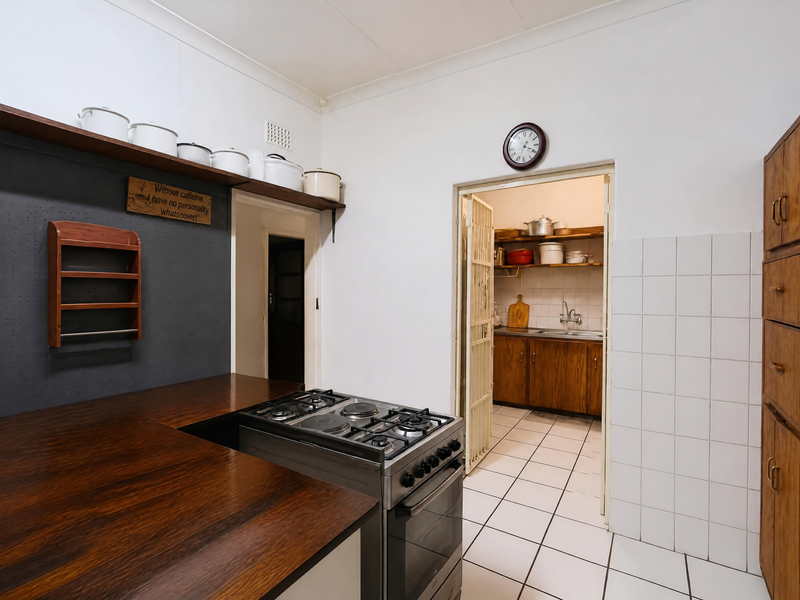 Kitchen featuring wooden countertops, a freestanding stove, and tiled flooring, with an adjacent scullery area visible through the doorway.