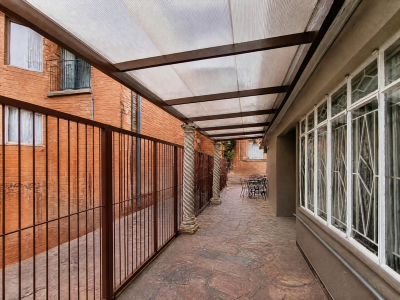 A covered outdoor patio area featuring stone flooring, decorative spiral columns, and a translucent roof, providing a sheltered transition space along the building exterior.