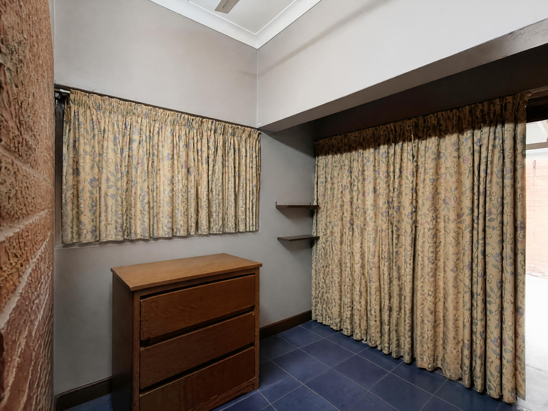 A bedroom featuring exposed brickwork, tiled flooring, and built-in shelving, with large curtains covering the window and closet areas.