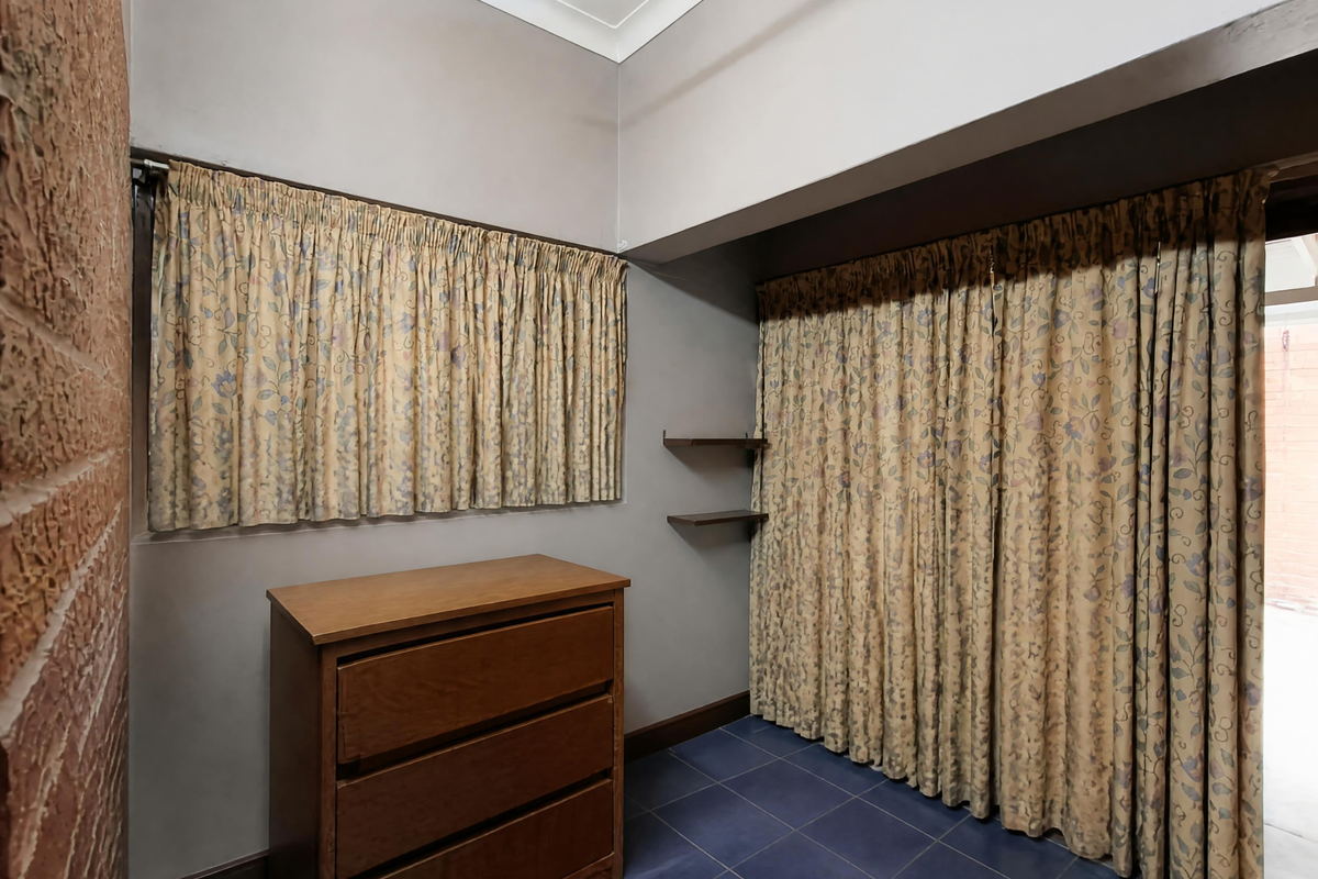 A bedroom featuring exposed brickwork, tiled flooring, and built-in shelving, with large curtains covering the window and closet areas.