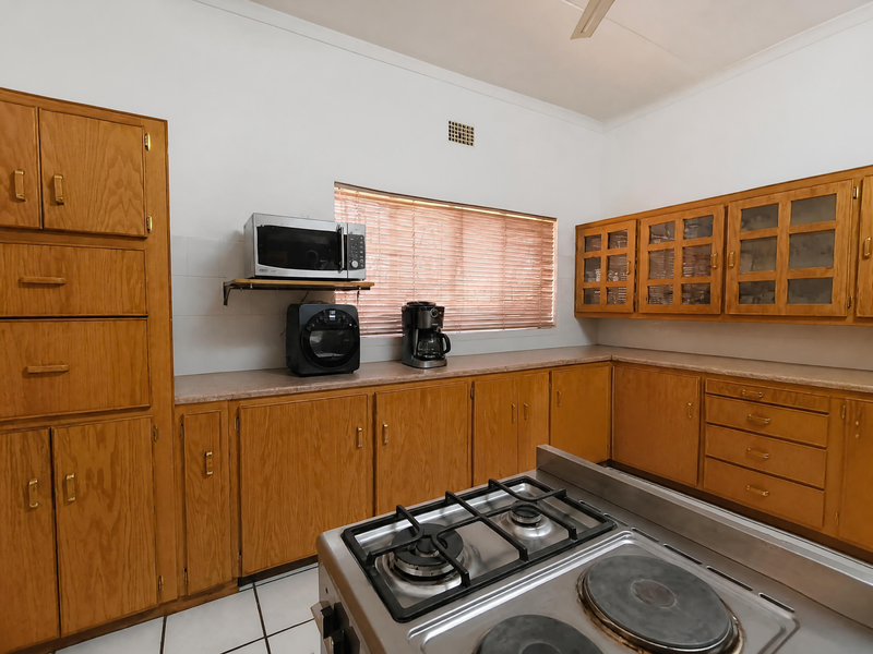 A functional kitchen featuring extensive wooden cabinetry, laminate countertops, and a combination gas and electric stove, complemented by tiled flooring and natural light.