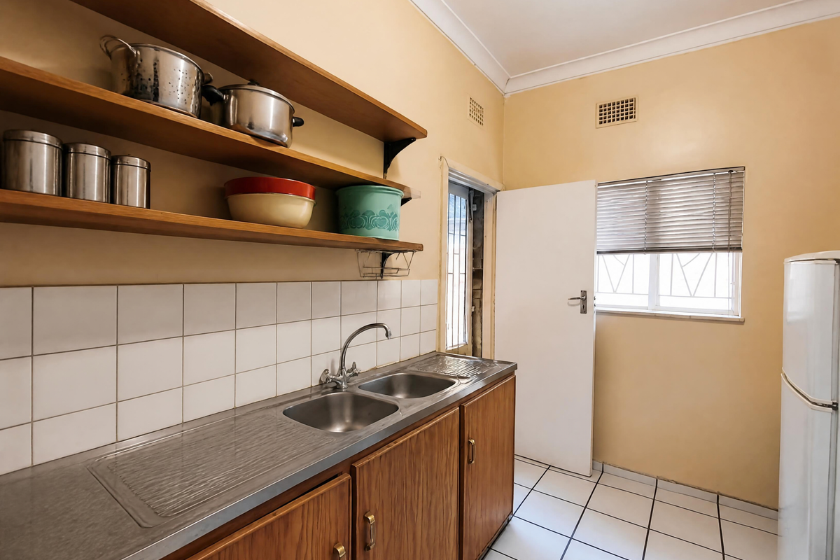 A functional kitchen featuring wooden cabinetry, open shelving, a double stainless steel sink, and tiled flooring with a neutral wall finish.