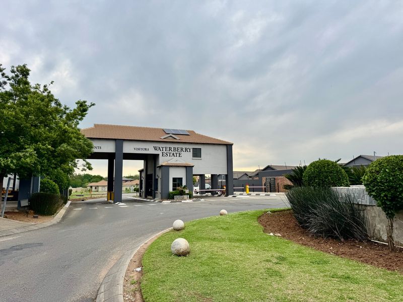 The entrance to Waterberry Estate featuring a modern security gatehouse, boom gate access, and well-maintained landscaped grounds.