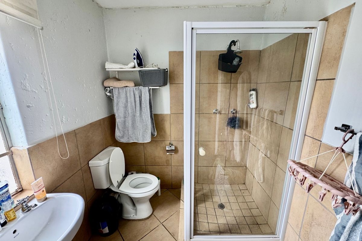 A functional bathroom featuring a shower enclosure, toilet, and pedestal basin with tiled finishes throughout.