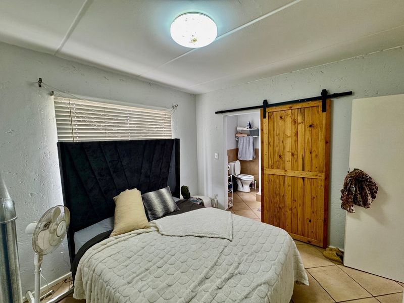 Bedroom featuring tiled flooring, a sliding wooden barn door leading to an en-suite bathroom, and venetian blinds.