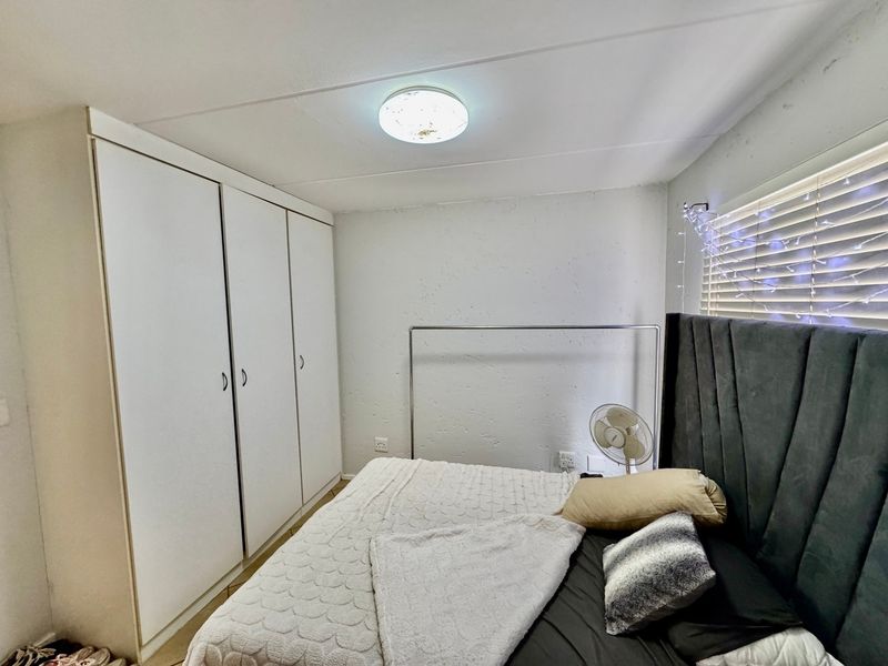 A bedroom featuring built-in cupboards, a ceiling light fixture, and venetian blinds, showing signs of wear on the walls and ceiling.