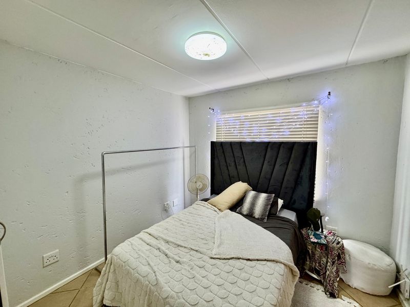 A bedroom featuring tiled flooring, textured walls, and a flush mount ceiling light with venetian blinds covering the window.
