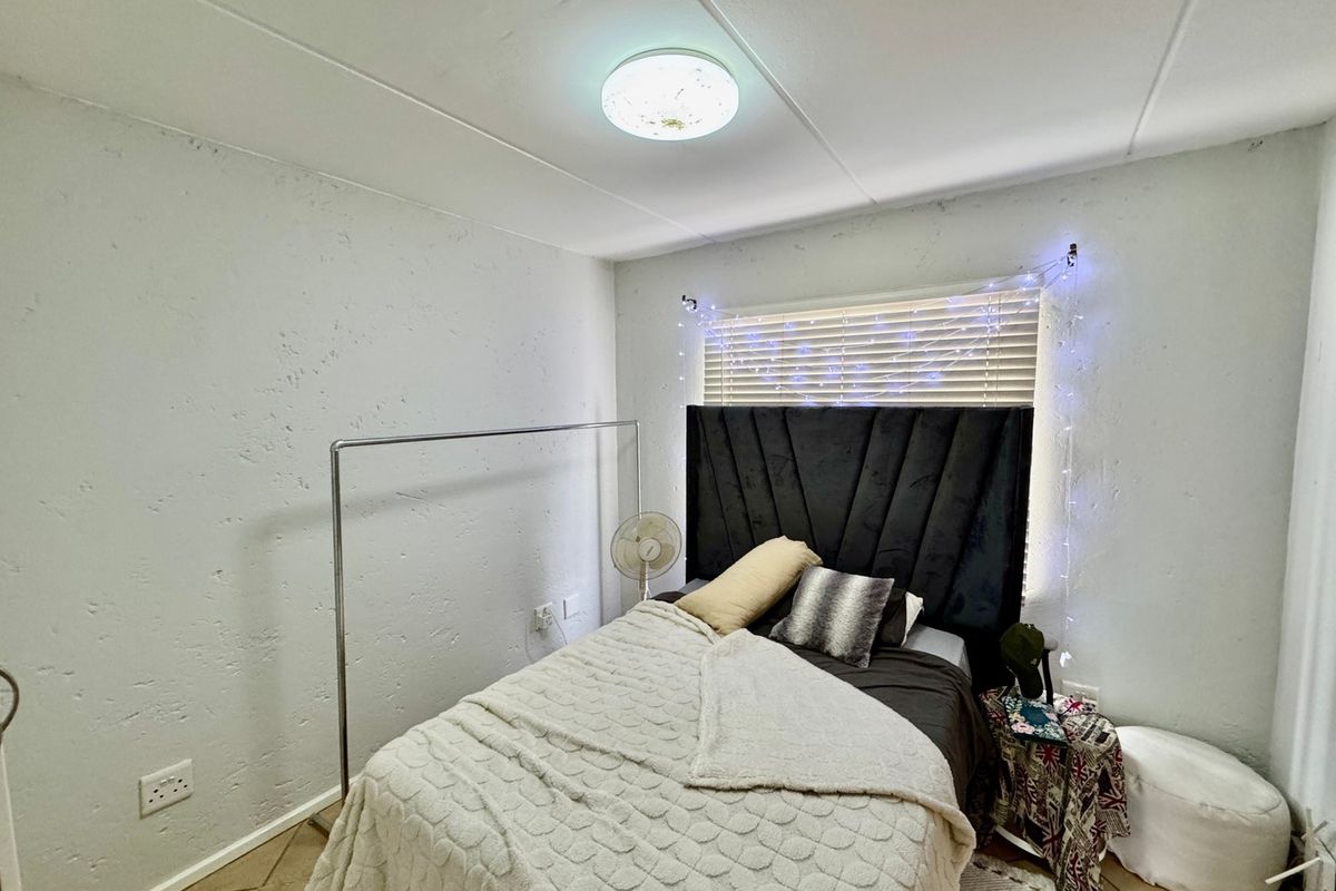 A bedroom featuring tiled flooring, textured walls, and a flush mount ceiling light with venetian blinds covering the window.