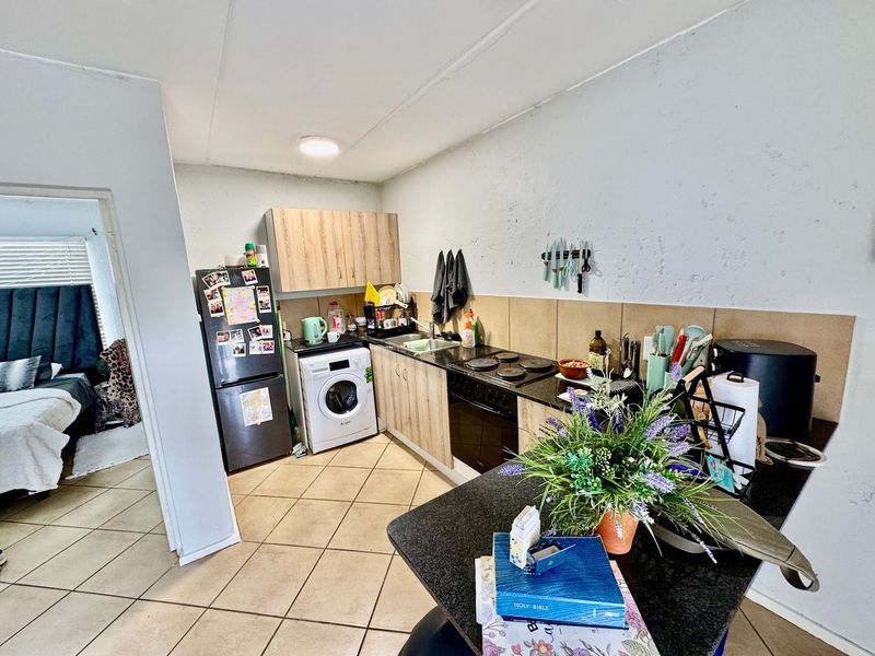 Compact kitchen featuring built-in cabinetry, laminate countertops, an electric hob, oven, and tiled backsplash, with direct access to an adjacent bedroom.