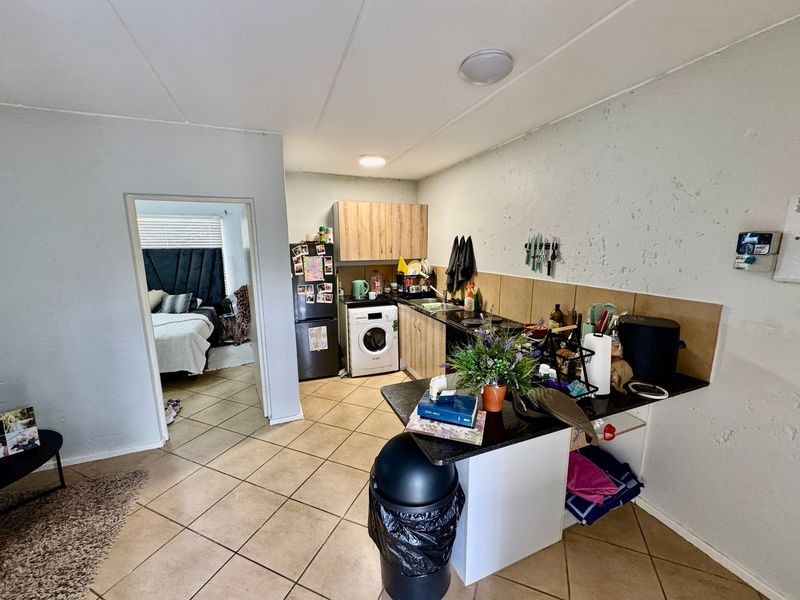 Open plan kitchen area featuring tiled flooring, built-in cabinetry, and a tiled backsplash, with direct access to the adjacent bedroom.