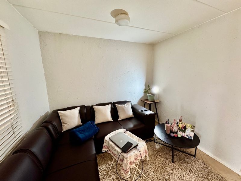 A compact living room area featuring textured walls and window blinds, offering a functional space for relaxation.