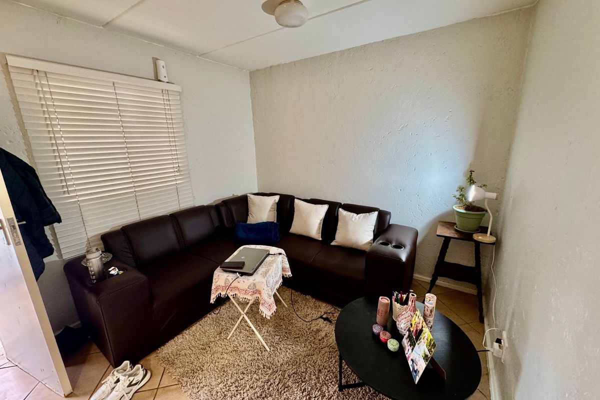 A compact living room featuring tiled flooring, venetian blinds, and a ceiling light fixture, offering a functional space with potential for cosmetic updates.