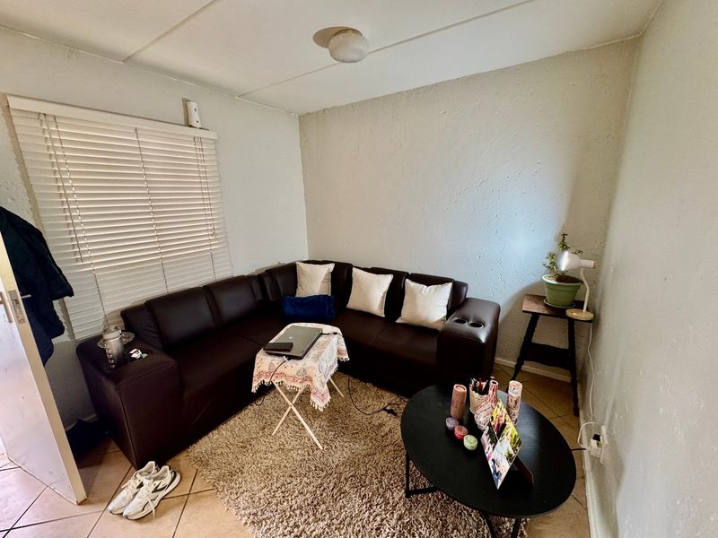 A compact living room featuring tiled flooring, venetian blinds, and a ceiling light fixture, offering a functional space with potential for cosmetic updates.