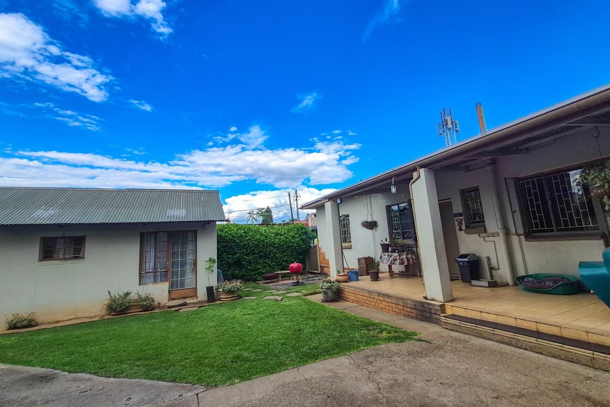 Rear view of the property featuring a lawn, a covered patio area with tiled flooring, and a separate outbuilding with a corrugated metal roof.