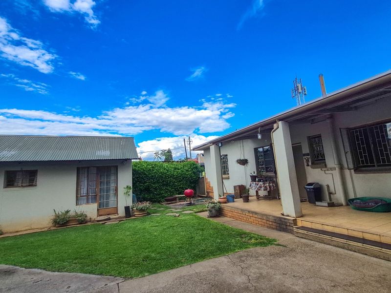 Rear view of the property featuring a lawn, a covered patio area with tiled flooring, and a separate outbuilding with a corrugated metal roof.