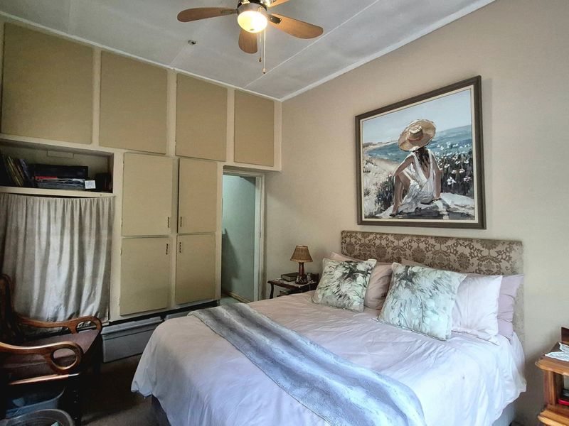 A bedroom featuring built-in cupboards and a ceiling fan, offering a functional space with potential for cosmetic updates.