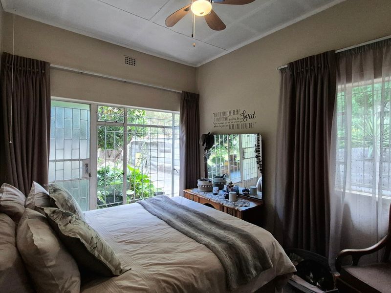 A cozy bedroom featuring a ceiling fan, large sliding glass doors with security gates, and windows fitted with security bars.