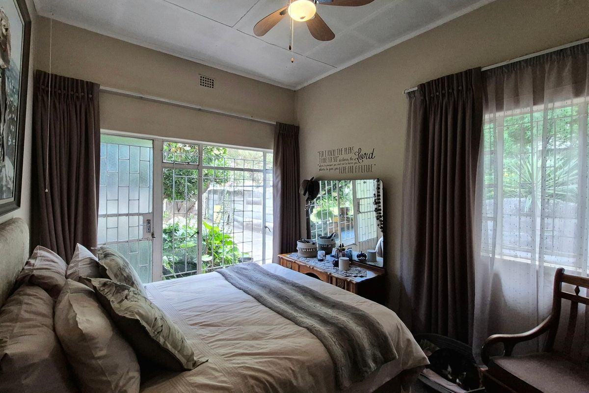 A cozy bedroom featuring a ceiling fan, large sliding glass doors with security gates, and windows fitted with security bars.