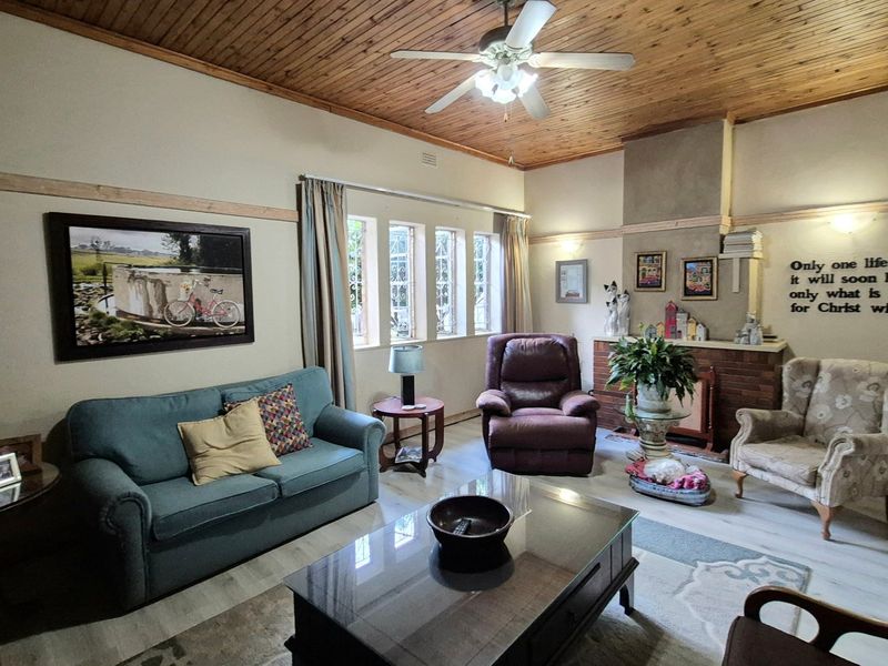 A cozy living room featuring a warm timber ceiling, a classic brick fireplace, and large casement windows that provide natural light.