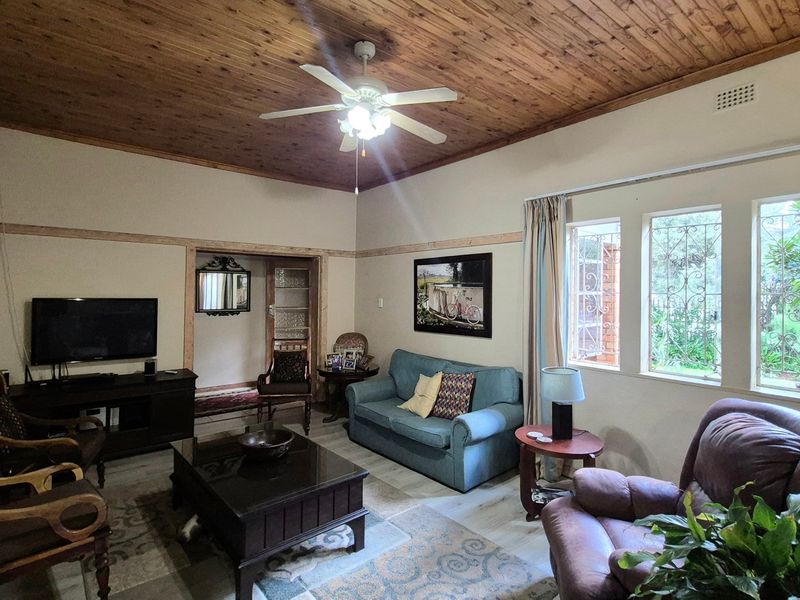 A comfortable living room featuring a warm timber tongue and groove ceiling, ceiling fan, and large windows with security bars.