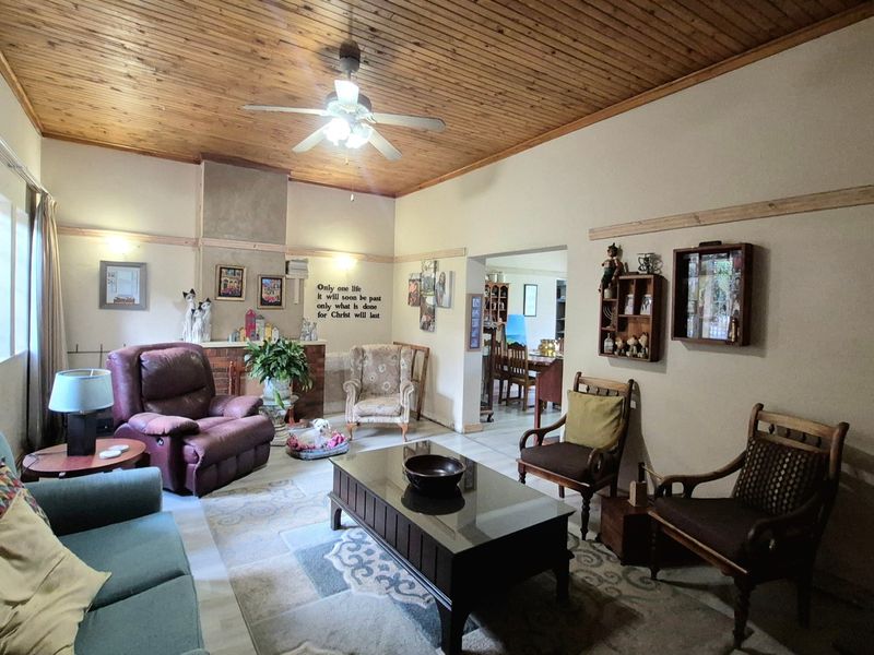 Spacious living room featuring a warm timber tongue and groove ceiling, ceiling fan, and a classic brick fireplace surround.
