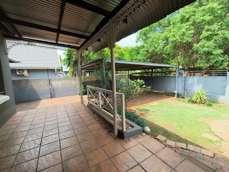 Covered patio area featuring tiled flooring and decorative ironwork, overlooking a private garden and carport space.
