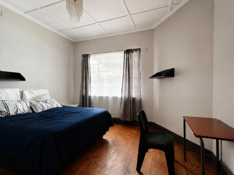 A bedroom featuring hardwood flooring, decorative ceiling paneling, and built-in wall shelving, offering a functional space with potential for cosmetic updates.