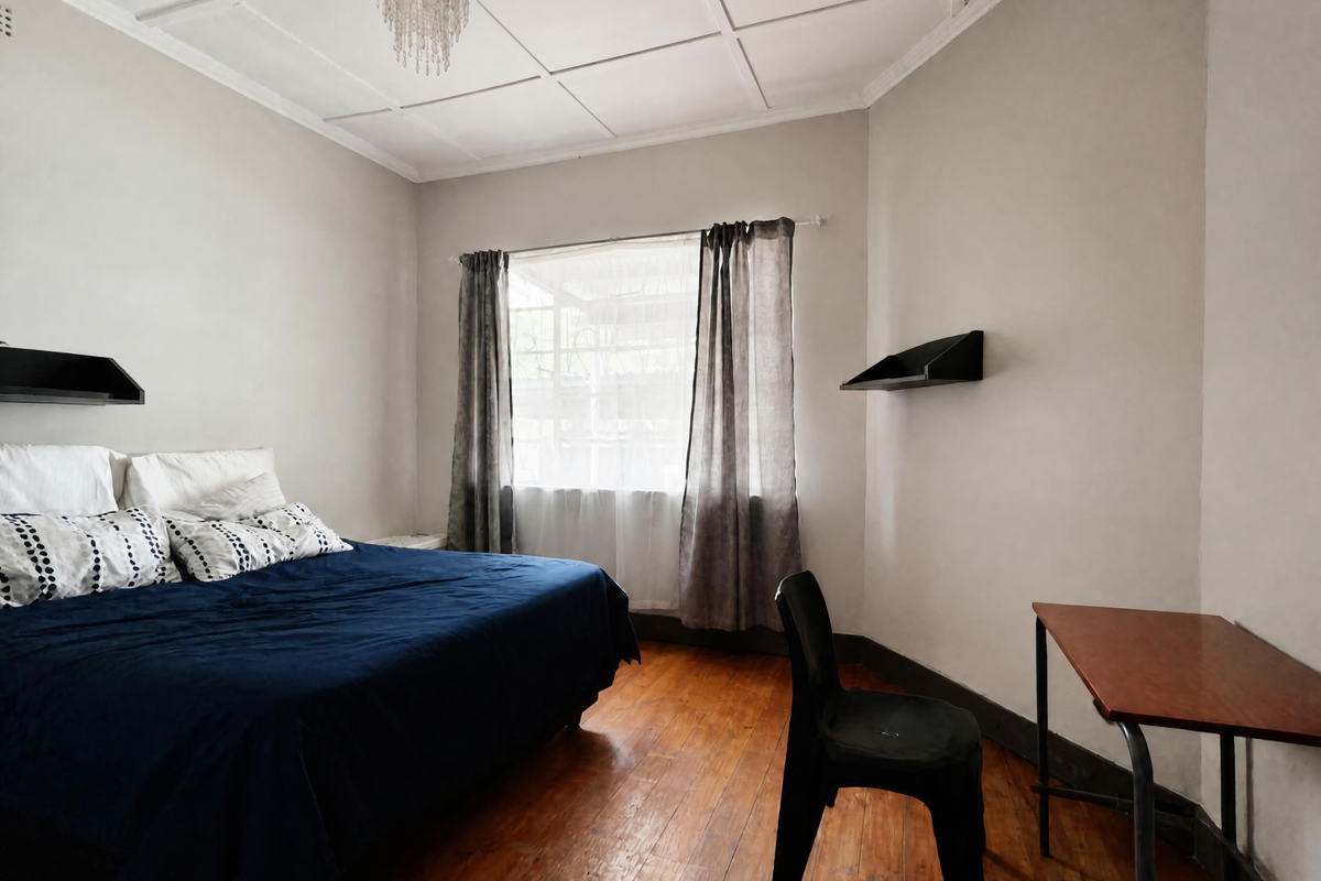 A bedroom featuring hardwood flooring, decorative ceiling paneling, and built-in wall shelving, offering a functional space with potential for cosmetic updates.
