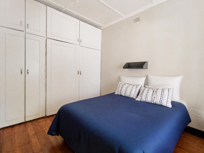 A well-maintained bedroom featuring classic wooden flooring, extensive built-in cupboard storage, and a clean, neutral aesthetic.