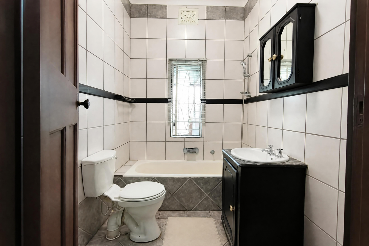 A functional bathroom featuring a built-in vanity, bathtub, toilet, and tiled finishes, offering a clean and practical layout.