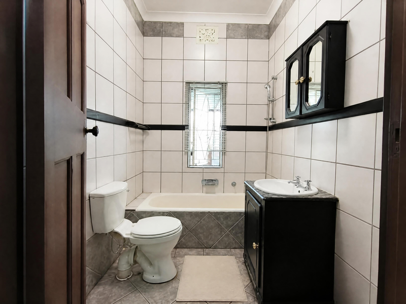 A functional bathroom featuring a built-in vanity, bathtub, toilet, and tiled finishes, offering a clean and practical layout.