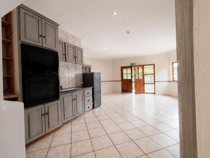 Spacious open-plan kitchen and living area featuring grey built-in cabinetry, tiled flooring, and direct access to the outdoors through wooden framed glass doors.