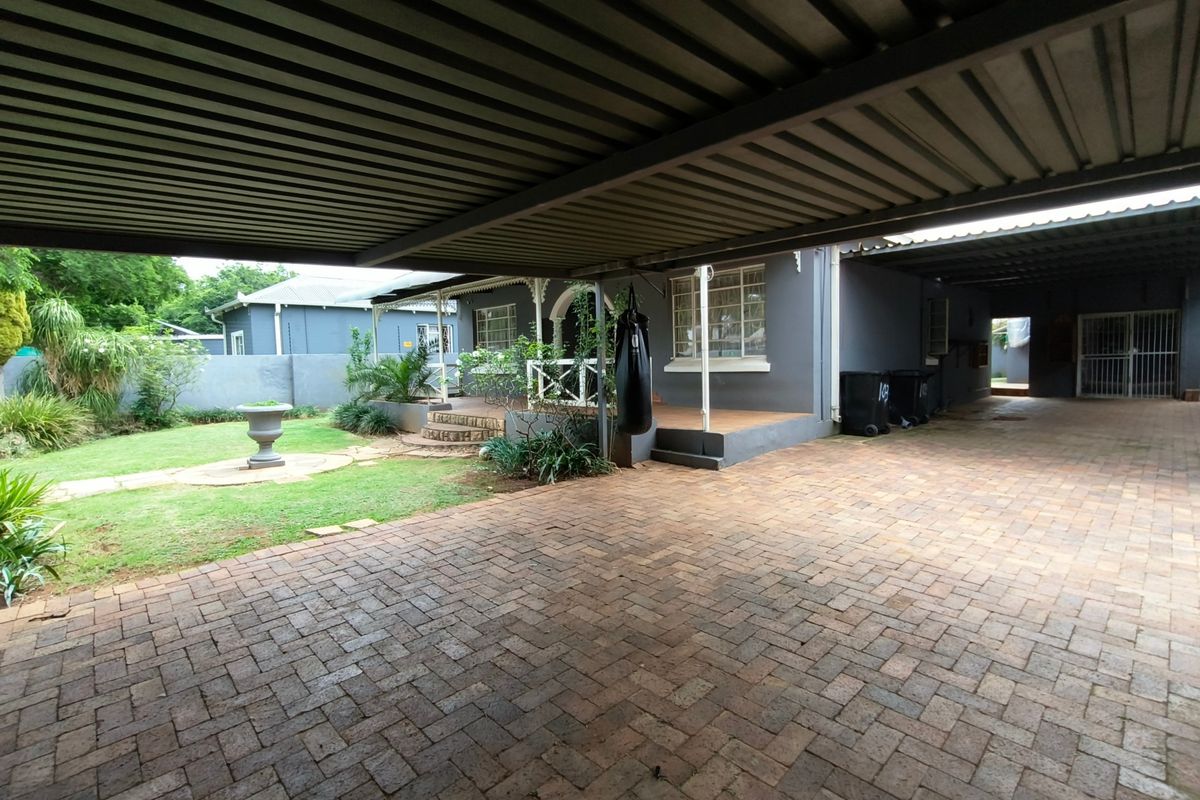 Spacious rear exterior featuring a large paved driveway, covered carport, and a covered patio area overlooking a landscaped garden.