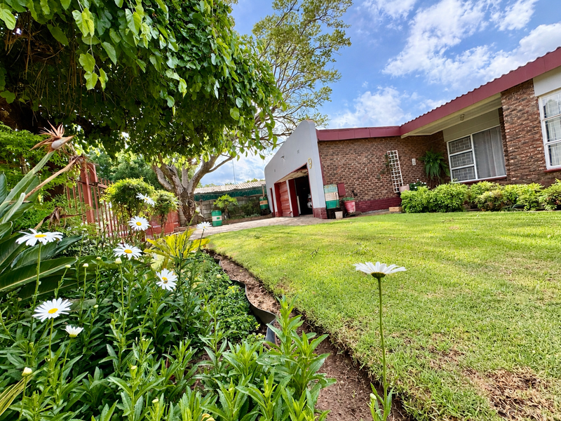 A well-maintained front garden with a lush lawn, mature tree, and brick facade featuring a garage and metal-framed windows.