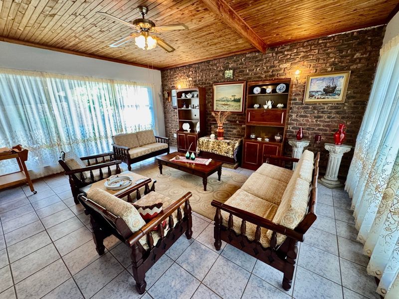 Spacious living room featuring a rustic exposed brick wall, timber ceiling with fan, and neutral ceramic floor tiles.