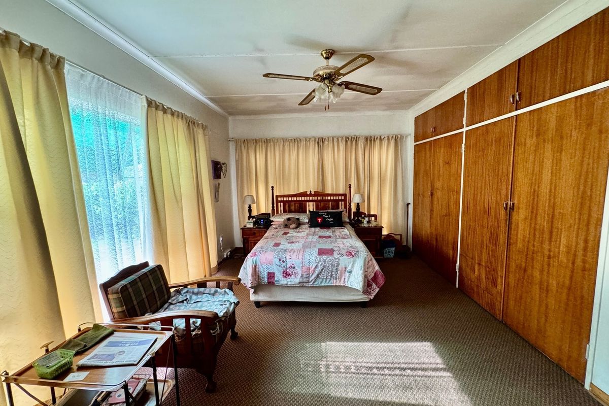 Spacious bedroom featuring extensive built-in wooden cabinetry, a ceiling fan, and large windows with natural light.