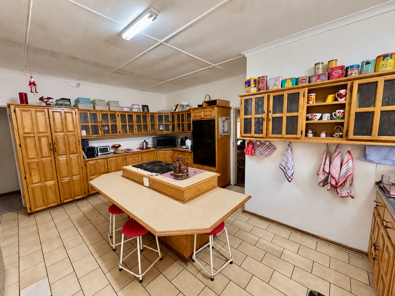 Spacious kitchen featuring extensive wooden cabinetry, a central island with a built-in hob, and tiled flooring, offering significant potential for a modern renovation.