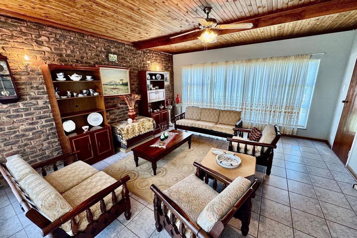 Spacious living room featuring a rustic exposed brick wall, warm timber ceiling, and neutral tiled flooring, offering a classic and comfortable atmosphere.