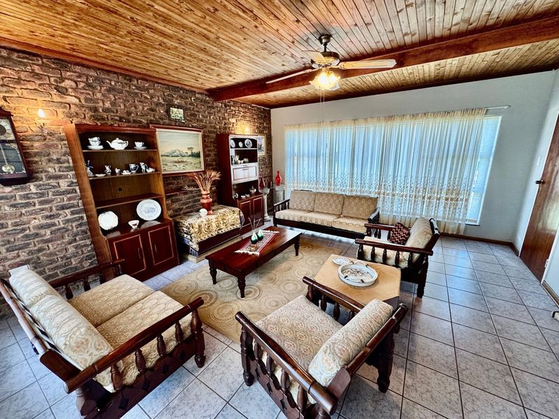 Spacious living room featuring a rustic exposed brick wall, warm timber ceiling, and neutral tiled flooring, offering a classic and comfortable atmosphere.