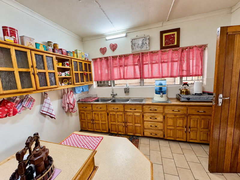 A functional kitchen featuring traditional wooden cabinetry, double basin sink, and tiled flooring, offering a classic layout with ample storage space.