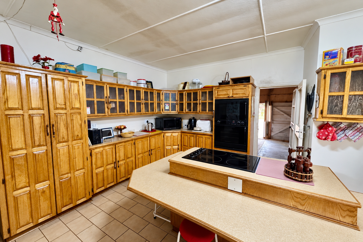 A spacious kitchen featuring extensive wooden cabinetry, a central island with a built-in electric cooktop, and tiled flooring.