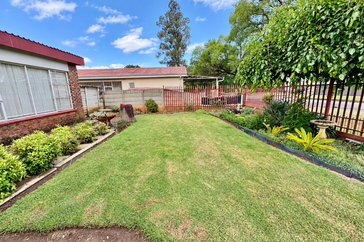 A well-maintained rear garden featuring a manicured lawn, established garden beds, and secure perimeter fencing with a concrete boundary wall.