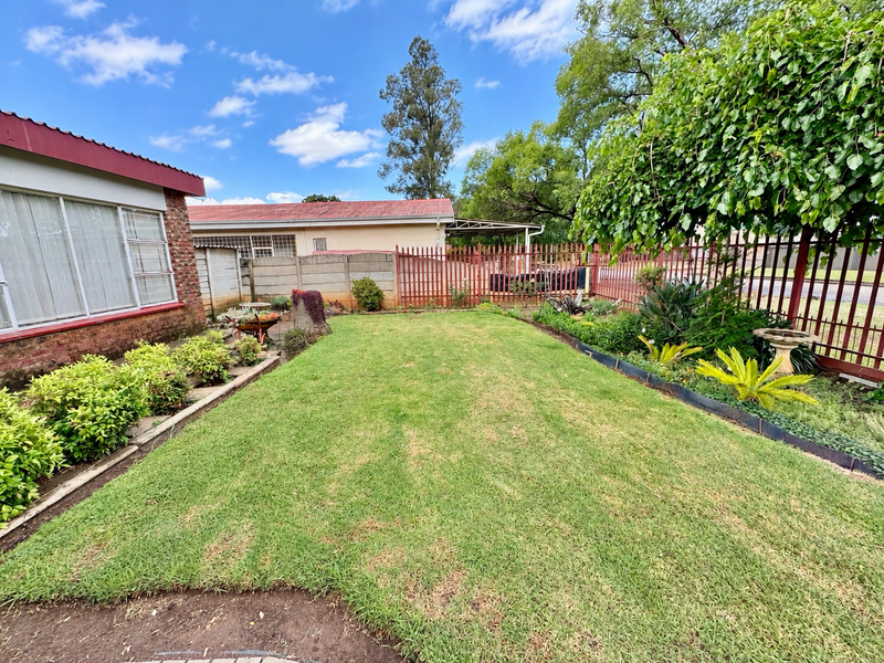 A well-maintained rear garden featuring a manicured lawn, established garden beds, and secure perimeter fencing with a concrete boundary wall.