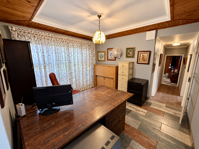 A functional home office featuring timber ceiling paneling, decorative cove cornicing, and durable tiled flooring, providing a practical workspace with access to the hallway.